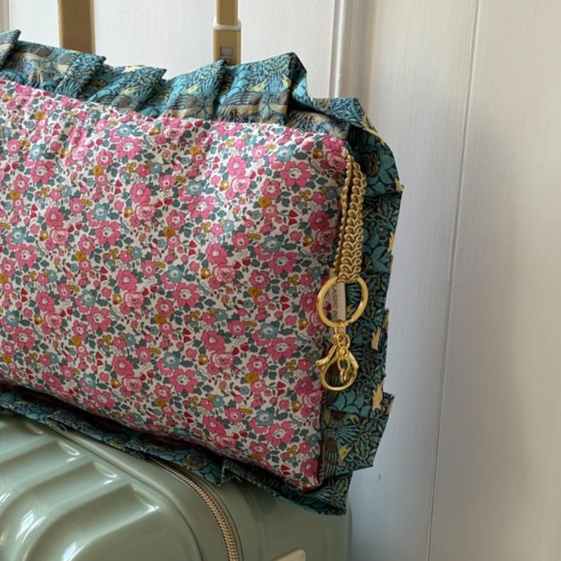 Floral-patterned travel bag on a suitcase against a white wall