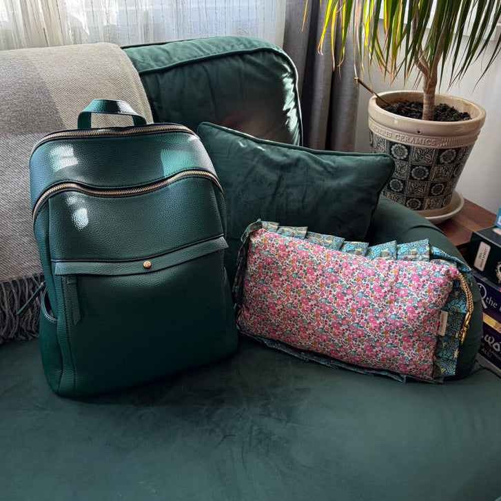 Green backpack and floral-patterned bag on a green couch with a plant in the background