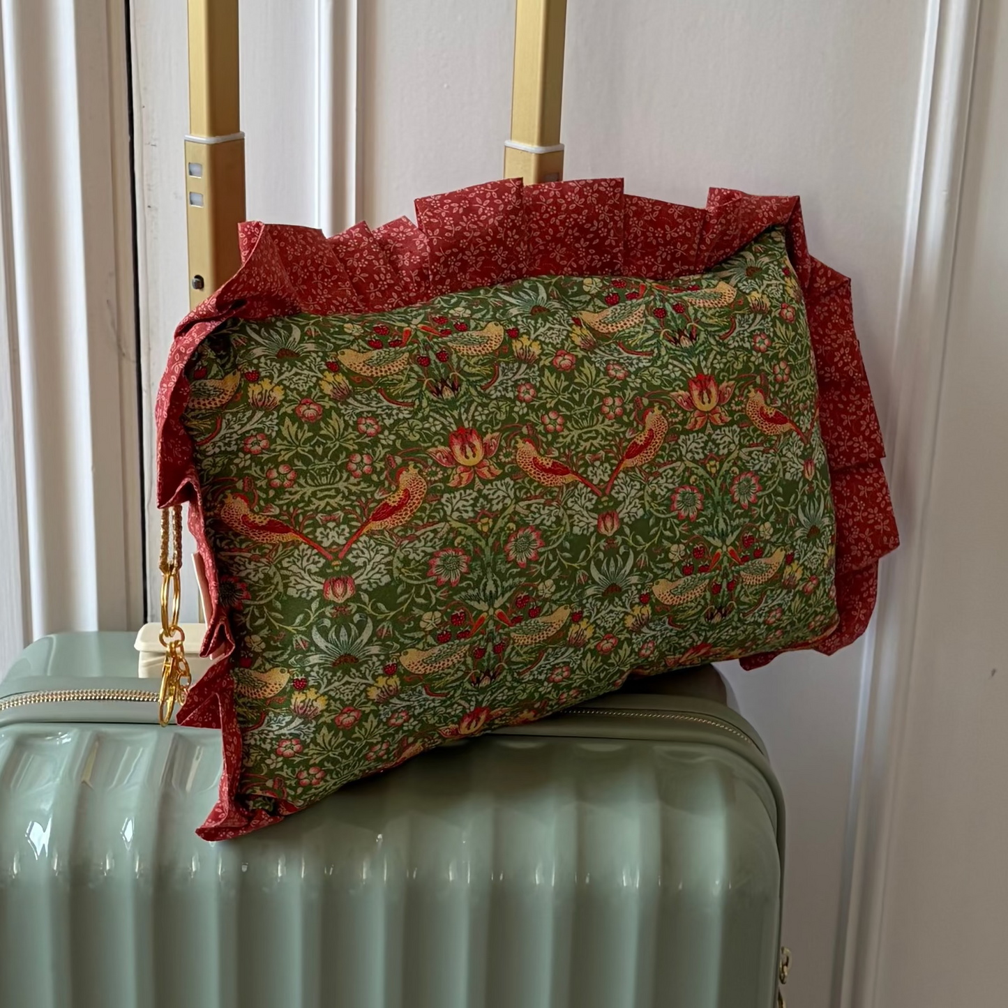 Green suitcase with a floral-patterned travel pillow on top in front of a white door.