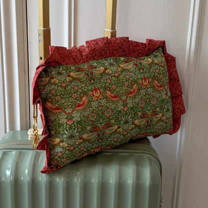 Green suitcase with a floral-patterned travel pillow on top in front of a white door.