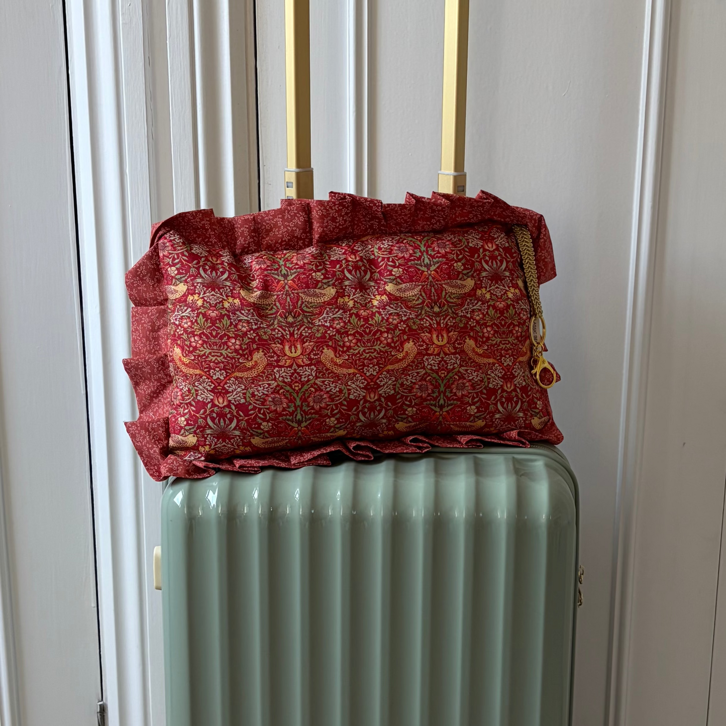 Green suitcase with a red william Morris pillow on top in front of white doors.