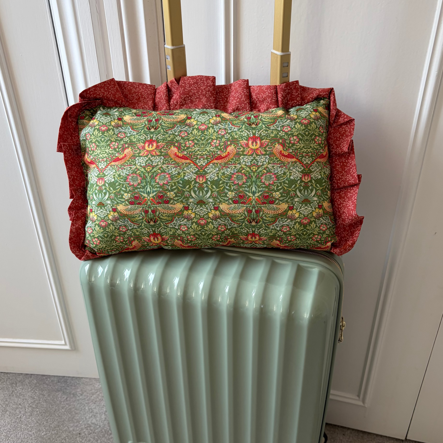 Green suitcase with a floral-patterned pillow on top against a white paneled wall.
