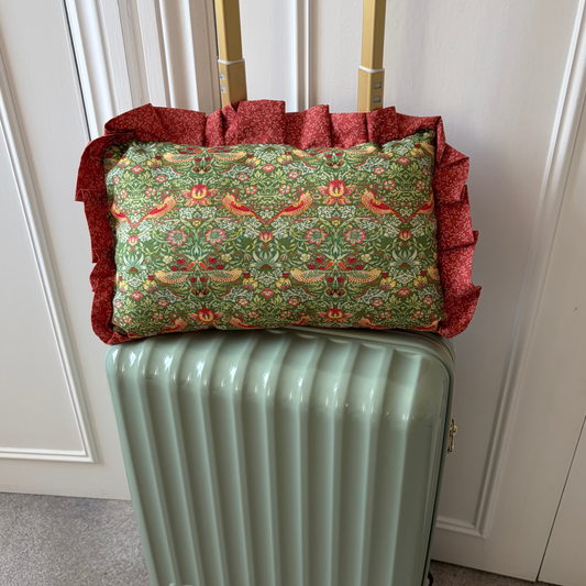 Green suitcase with a floral-patterned pillow on top against a white paneled wall.