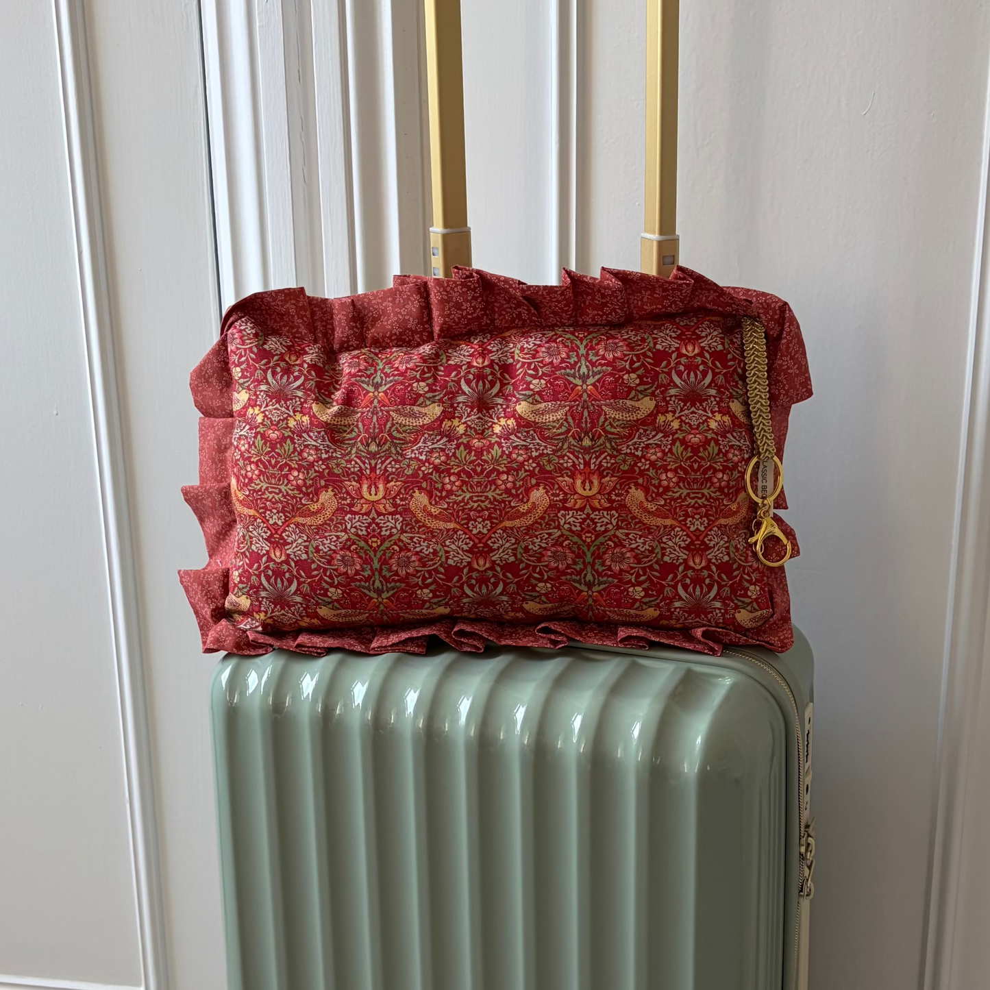 Green suitcase with a red william morris pillow on top in front of a white door.