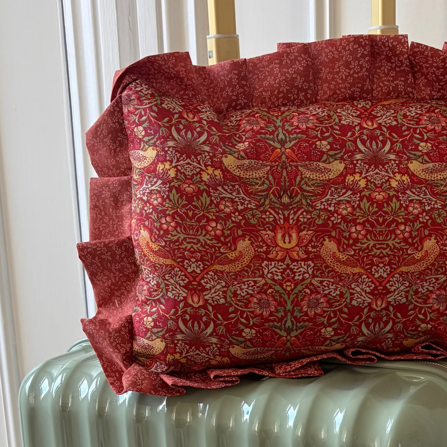 Green suitcase with a red patterned pillow on top against a white wall.