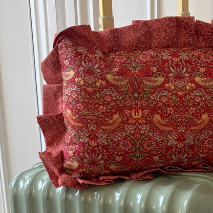 Green suitcase with a red patterned pillow on top against a white wall.
